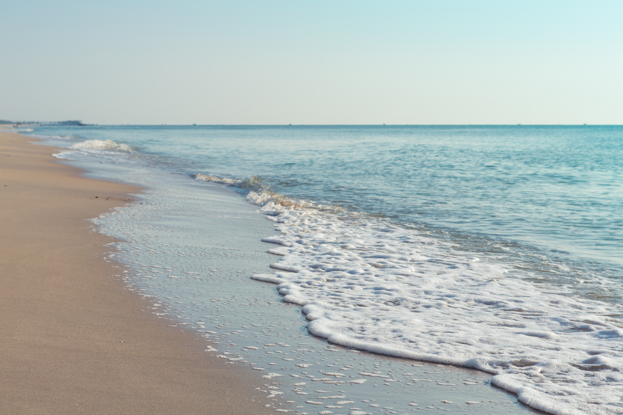 Calm ocean waves on sandy beach shore.